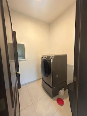 A compact laundry room with a front-loading washer and dryer, a small window, and a red bowl on the floor.