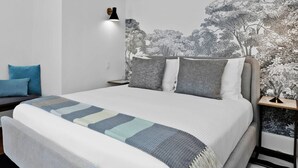 A bed with a patterned blanket, a nightstand with a lamp, and a wall with a nature-themed mural. - A Private Guesthouse Studio – The Otter (Napa)