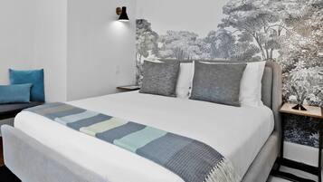 A bed with a patterned blanket, a nightstand with a lamp, and a wall with a nature-themed mural.