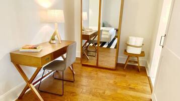 A room with a wooden desk, a chair, a lamp, a mirror, and a small stool.