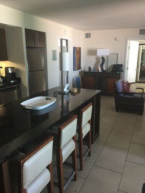 Uma cozinha moderna com frigorífico, fogão e máquina de café. Possui uma área de refeições com mesa e cadeiras.