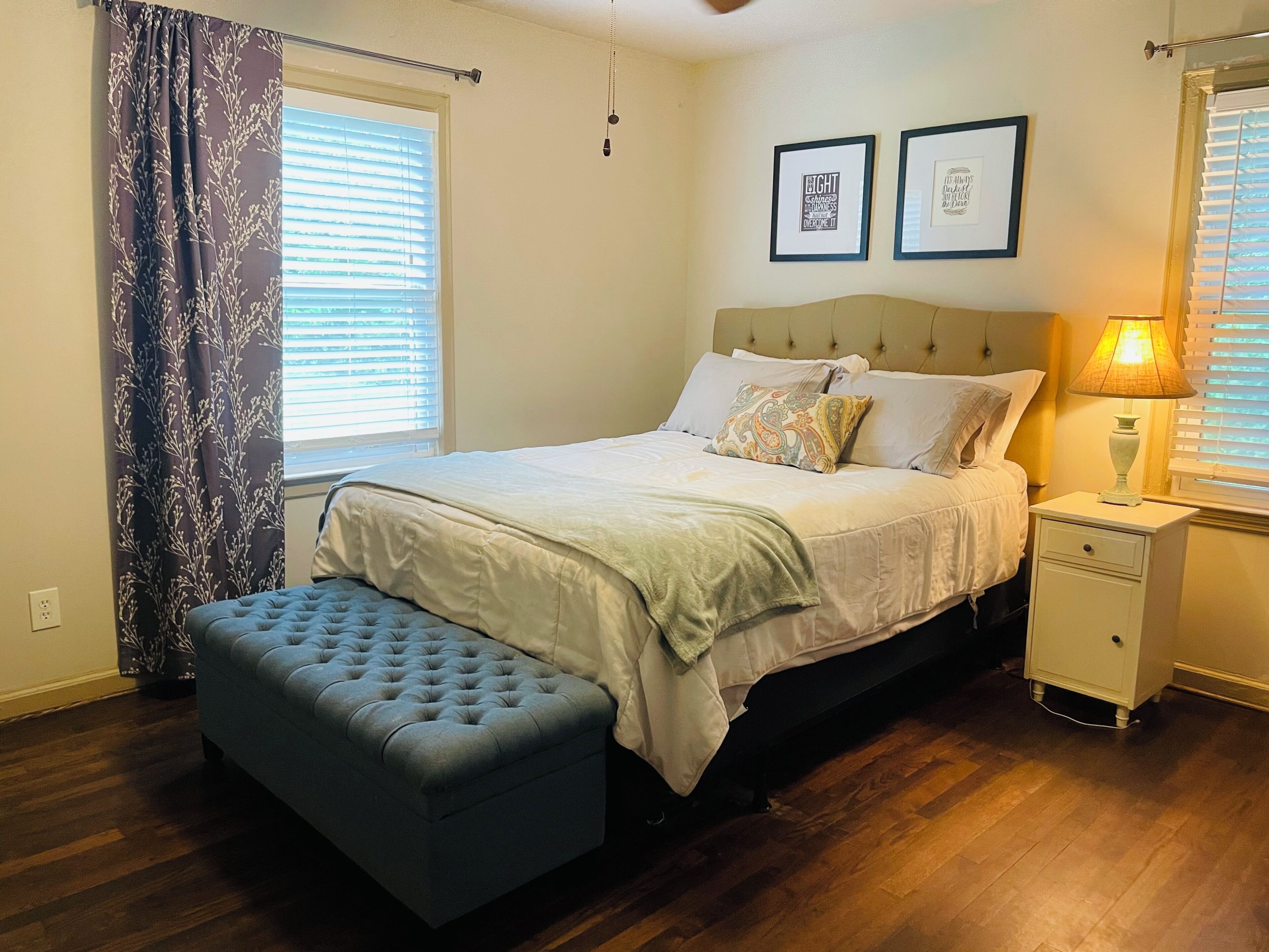 A bedroom with a bed, bedside table, lamp, and a window with blinds.