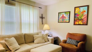 A living room with a beige sofa, an ottoman, a patterned rug, a side table with a lamp, and two framed artworks on the wall. - Pet-Friendly Home Near Dragon Con & Downtown (Atlanta)