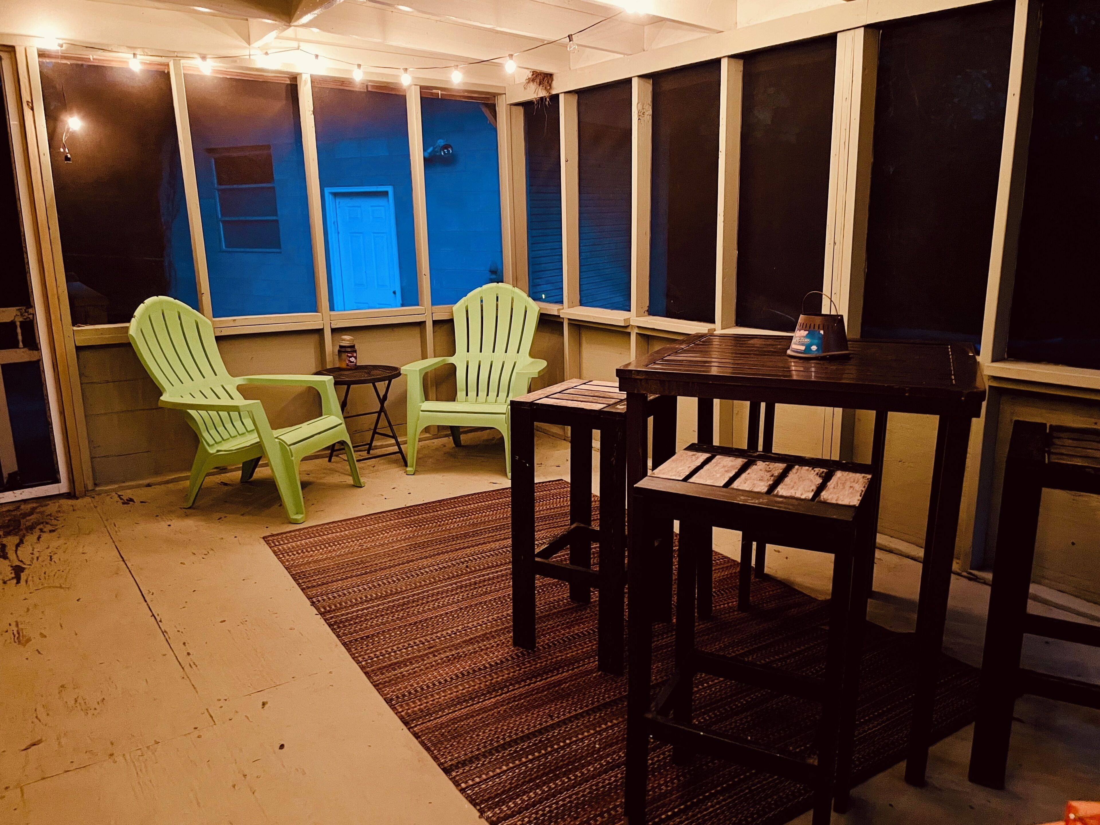 Een kamer met een tafel, twee stoelen, een kleedje en een raam met uitzicht op een gebouw.