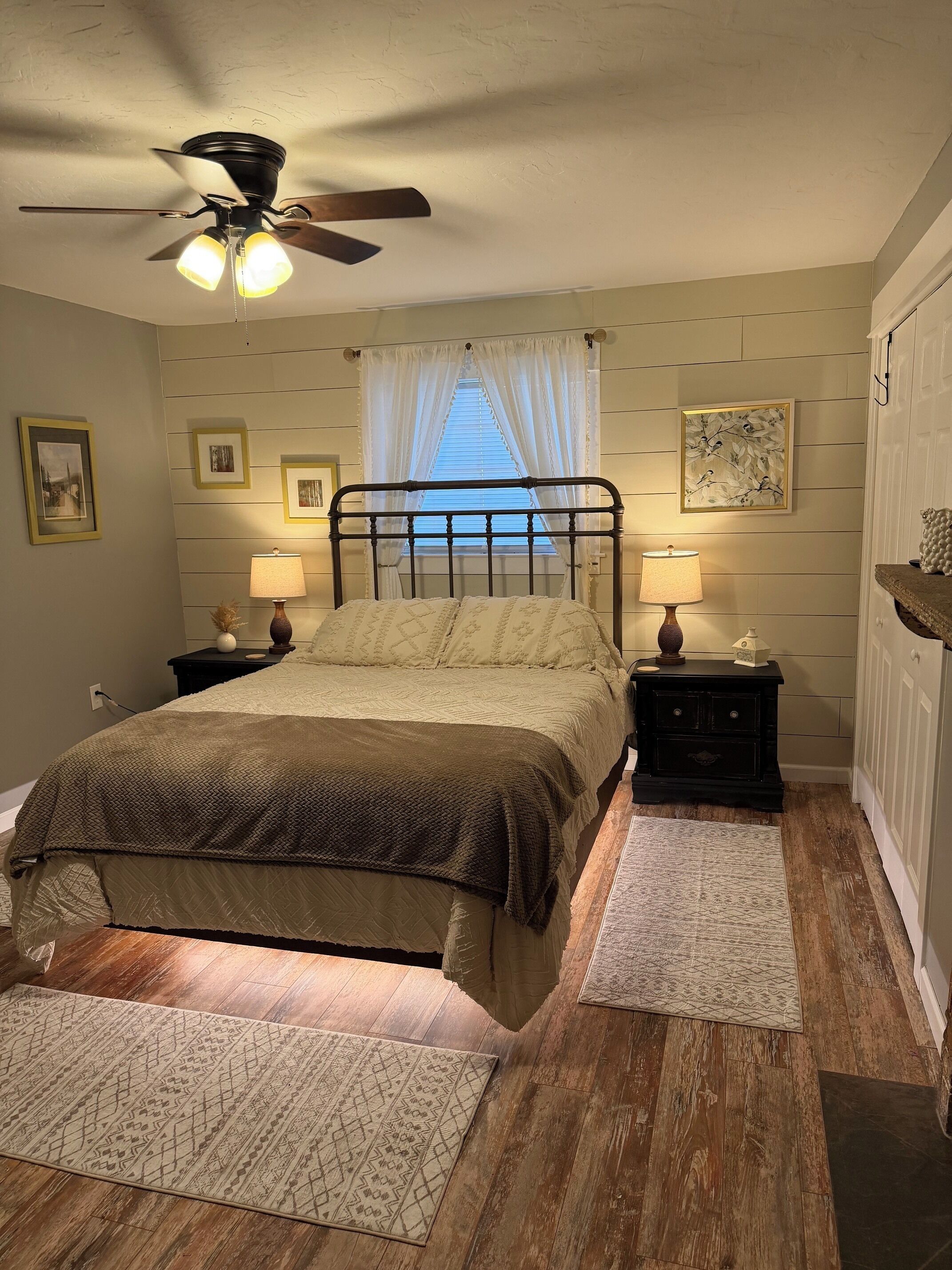 A bedroom with a bed, two bedside tables, a ceiling fan, and a window with curtains.