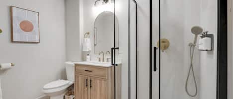 A modern bathroom with a glass-enclosed shower, a toilet, a sink with a mirror, and a framed artwork on the wall.