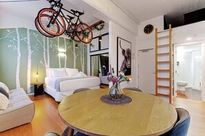 A modern bedroom with a bed, a round dining table with a vase of flowers, and a bicycle hanging from the ceiling. - Central CBD Studio with Projector Cinema Loft (Auckland CBD)