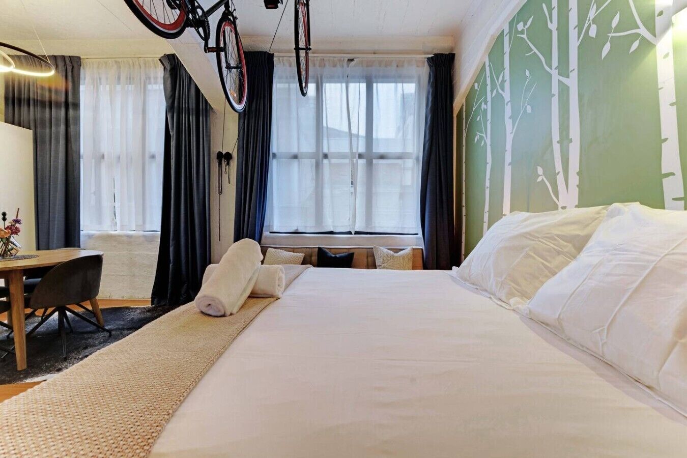 A hotel room with a large bed, a desk, and a bicycle hanging from the ceiling.