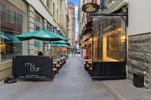 A narrow street with outdoor seating, a bar sign, and a storefront. - Central CBD Studio with Projector Cinema Loft (Auckland CBD)