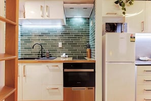 A compact kitchen with white cabinetry, a black dishwasher, and a green-tiled backsplash. - Central CBD Studio with Projector Cinema Loft (Auckland CBD)