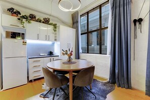 A compact kitchen with white cabinets, a built-in oven, and a dining area with a round table and chairs. - Central CBD Studio with Projector Cinema Loft (Auckland CBD)