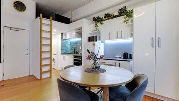 A compact kitchen with white cabinets, a wooden dining table with chairs, and a small plant on the counter.