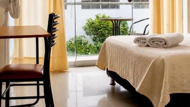 Una habitació d'hotel amb un llit, una cadira, una taula i una finestra amb cortines.
