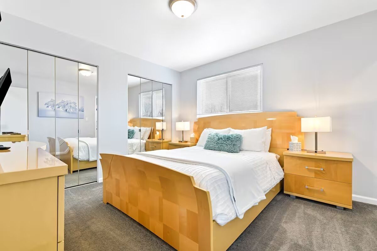 A hotel room with a bed, bedside tables, a desk, a mirror, and a window.