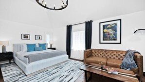 A modern hotel room with a bed, a sofa, a wooden coffee table, and a chandelier.