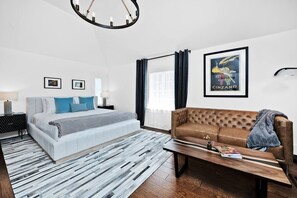 A modern hotel room with a bed, a sofa, a wooden coffee table, and a chandelier.