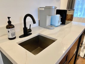A kitchen with a built-in sink, a coffee maker, and a bottle of hand soap.
