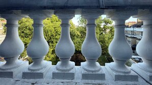 Ein Balkon mit weißen Geländern, der auf eine Stadtansicht mit Bäumen und Gebäuden blickt.