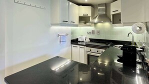 Eine moderne Küche mit weißen Schränken, einer schwarzen Arbeitsplatte, Edelstahlgeräten und einem an der Decke befestigten Rauchmelder.