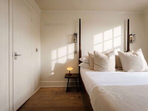 Een hotelkamer met een bed, een nachtkastje met een lamp en een raam met zonlicht.