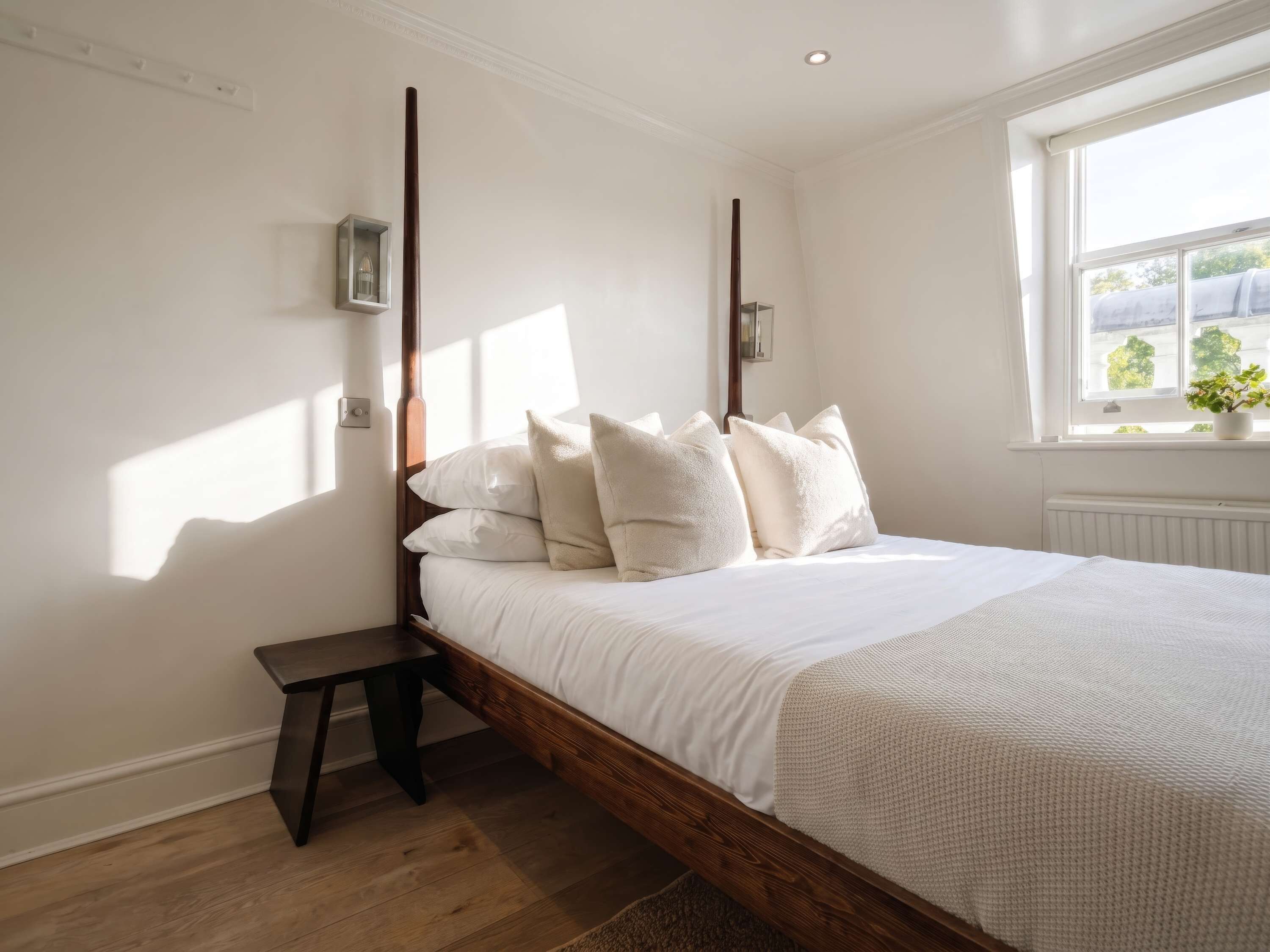 Une chambre à coucher avec un lit en bois, du linge de lit blanc, une table de chevet, une lampe fixée au mur et une fenêtre donnant sur un beau paysage.