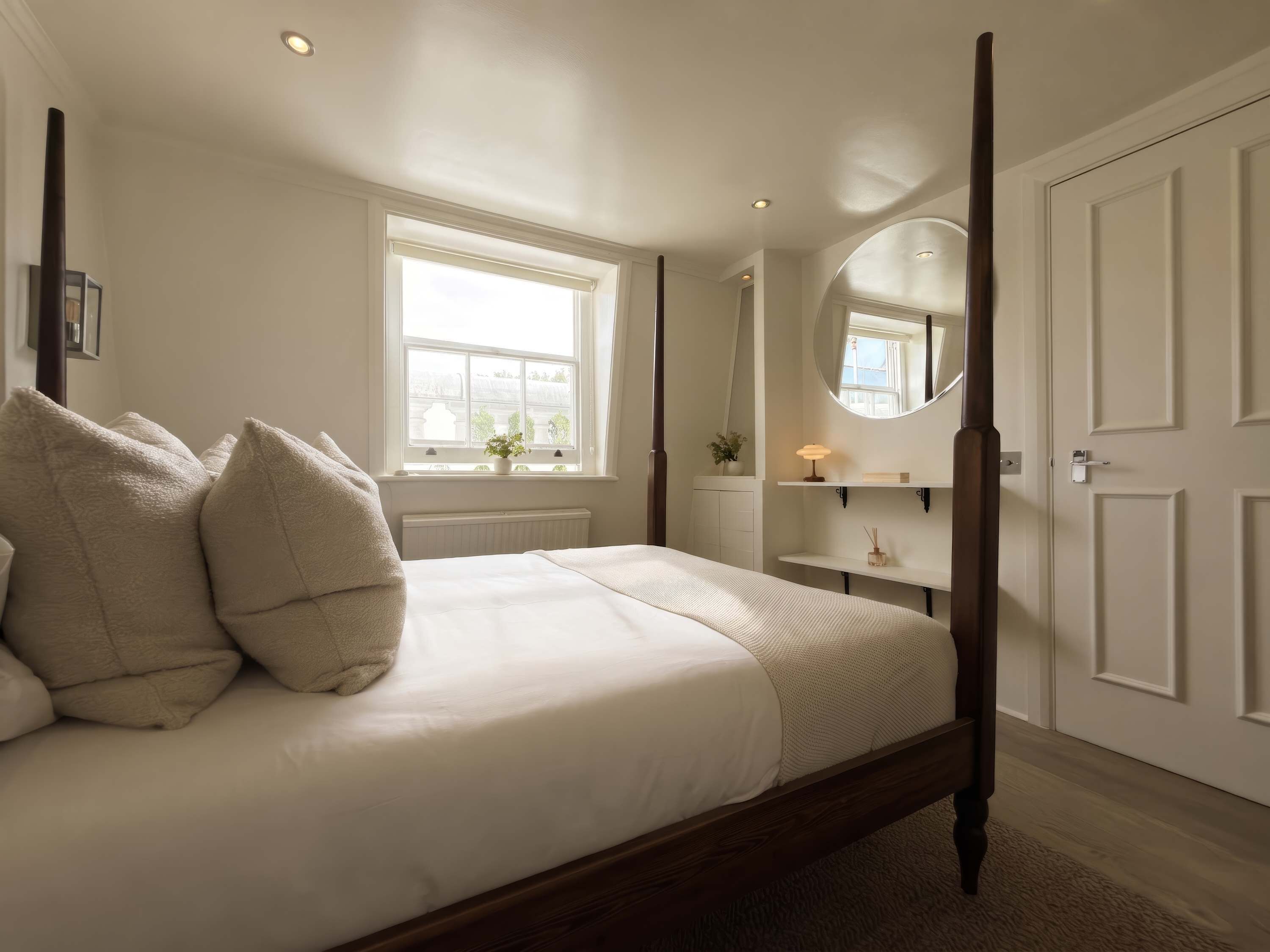 Een slaapkamer met een hemelbed, een raam met uitzicht, een nachtkastje met een lamp, en een deur.