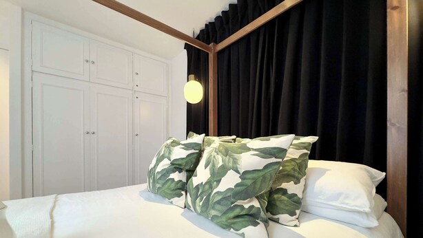 Un lit avec une literie blanche et deux oreillers à motifs de camouflage, une tête de lit en bois et une armoire blanche à deux portes.
