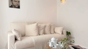 Un salon aux couleurs neutres, avec un canapé, une table basse sur laquelle se trouve un vase blanc et une télécommande, ainsi qu’un luminaire fixé au mur.