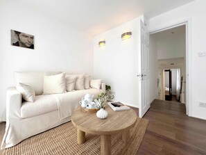 A minimalist living room with a beige sofa, a round wooden coffee table, and a white vase with flowers. - Chic Marble Arch w/ 100" Cinema & Premium Mattress (London)