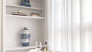 A dining area with a round wooden table, white plates, wine glasses, and a blue and white vase on a shelf. - Chic Marble Arch w/ 100" Cinema & Premium Mattress (London)