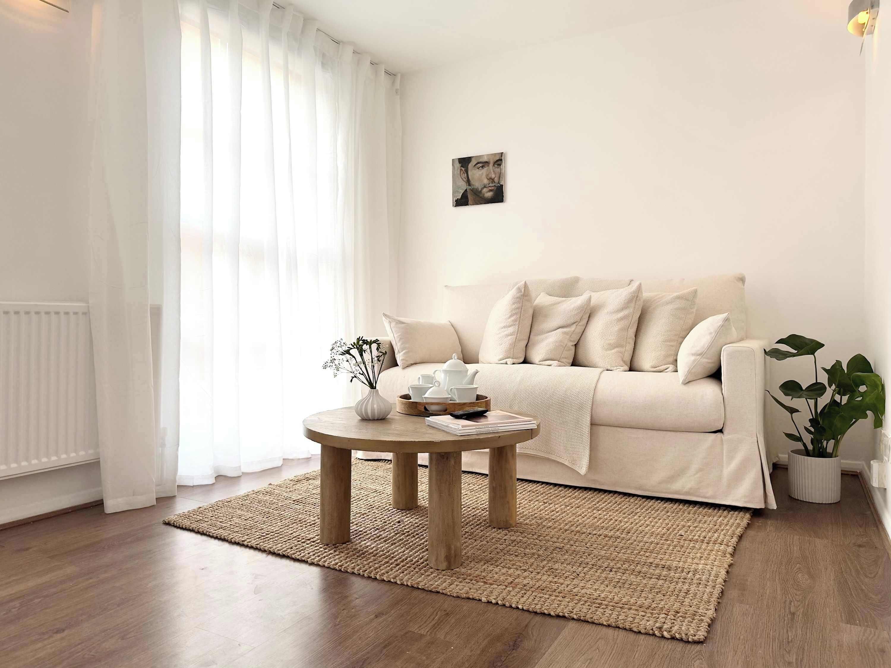 A minimalist living room with a beige sofa, a round wooden coffee table, and a potted plant.