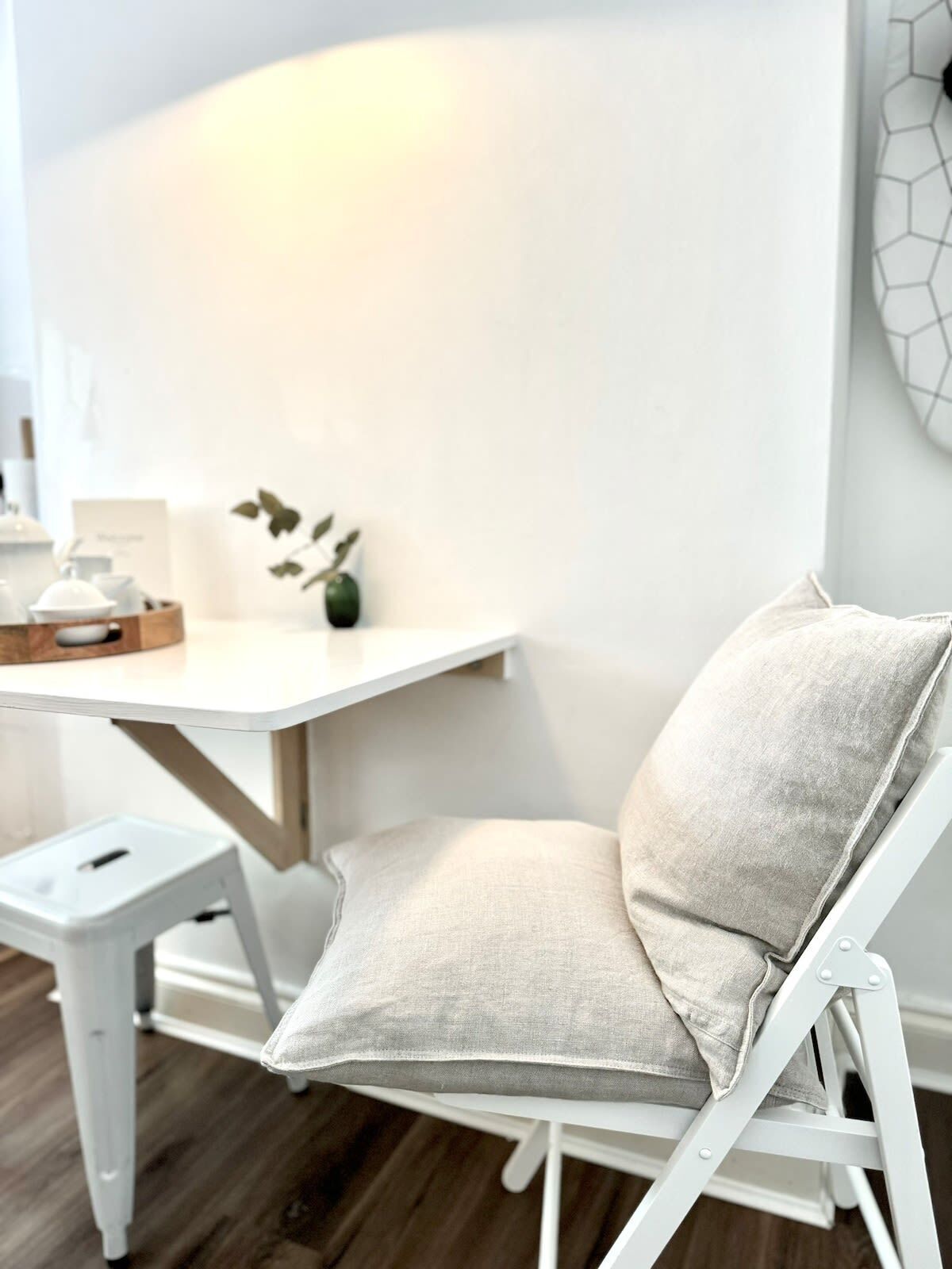 Une chaise blanche avec un coussin, un petit tabouret blanc et une table blanche ornée d’une plante et d’une boîte.