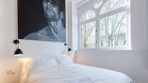 A bedroom with a bed, a window with a view, and a painting on the wall. - St. Luke's View, Shoreditch, by the Design Traveller (London)