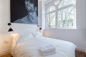 A bedroom with a bed, a window with a view, and a painting on the wall. - St. Luke's View, Shoreditch, by the Design Traveller (London)