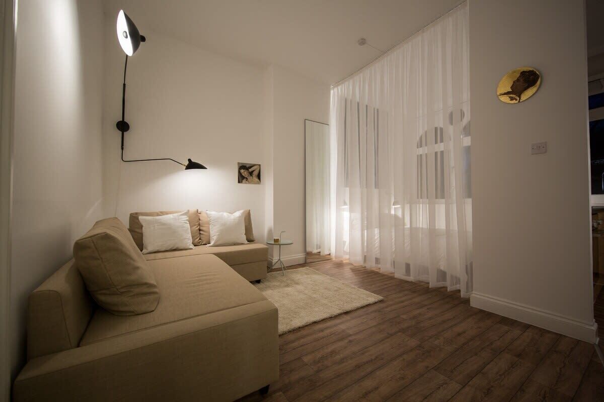 A modern living room with a sofa, a lamp, a small table, and sheer curtains.