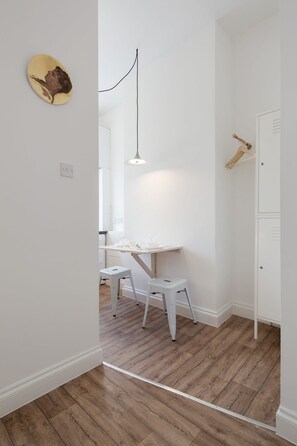 A room with a desk, two stools, a hanging light fixture, and a wardrobe. - St. Luke's View, Shoreditch, by the Design Traveller (London)