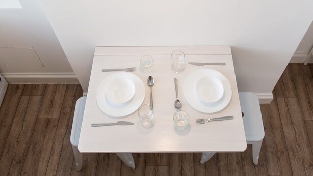 A dining table set with plates, cutlery, and glasses, under a pendant light. - St. Luke's View, Shoreditch, by the Design Traveller (London)