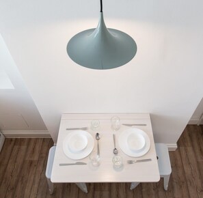 A dining table set with plates, cutlery, and glasses, under a pendant light. - St. Luke's View, Shoreditch, by the Design Traveller (London)