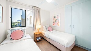 Quarto com duas camas, uma janela, um ventilador de teto e um guarda-roupa.