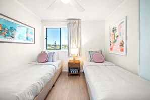 Un dormitorio con dos camas individuales, una ventana con cortinas y obras de arte en las paredes.