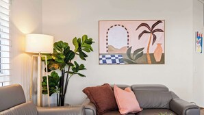 Uma sala de estar moderna com um sofá cinzento, uma luminária de chão e uma obra de arte na parede.