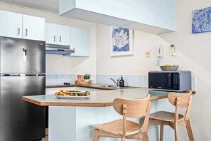 A modern kitchen with a stainless steel refrigerator, a microwave, and a wooden island with chairs. - Passage Panorama - 3BD Seaview Retreat (Caloundra Region)