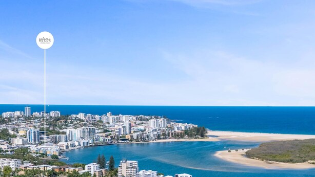 Paisagem costeira com uma mistura de edifícios residenciais e comerciais, céu azul claro e mar calmo.