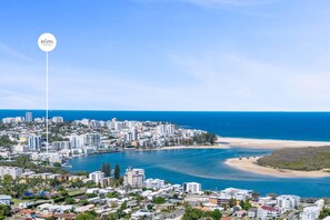 A coastal cityscape with a mix of residential and commercial buildings, a clear blue sky, and a calm sea. - Passage Panorama - 3BD Seaview Retreat (Caloundra Region)