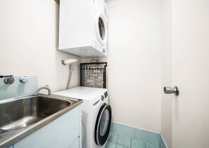 A compact laundry area with a washing machine, a dryer, and a sink. - Passage Panorama - 3BD Seaview Retreat (Caloundra Region)