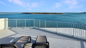 Um terraço com duas espreguiçadeiras de frente para um mar calmo e uma ilha distante.