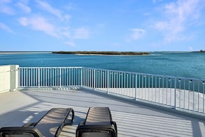 Eine Terrasse mit zwei Liegestühlen, die auf ein ruhiges Meer und eine entfernte Insel blicken.