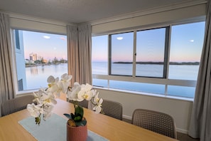 A hotel room with a dining table, chairs, and a view of a body of water and cityscape.