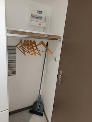 Una habitación con pared blanca, perchero de madera, escoba y termostato.