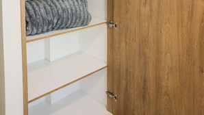 Ein Holzkleiderschrank mit drei Einlegeböcken, einer mit einem zusammenrollten weißen Bettlaken und ein anderer mit einem grauen, gemusterten Gegenstand.